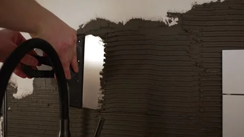 Professional tiler applying adhesive with a notched trowel on a wall, preparing Stock Footage 344564605