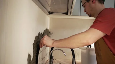Professional tiler installing ceramic backsplash tiles on kitchen wall with Stock Footage 344569899