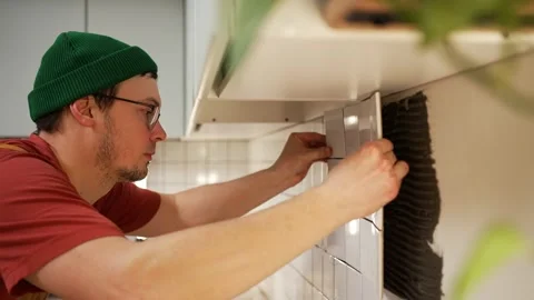 Professional tiler installing white ceramic backsplash tiles on a kitchen wall Stock Footage 330198646