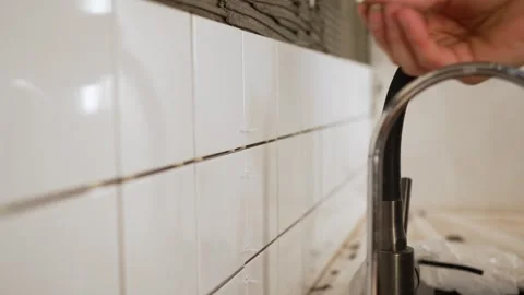 Professional tiler installing white ceramic tiles on a kitchen wall using Stock Footage 344563903