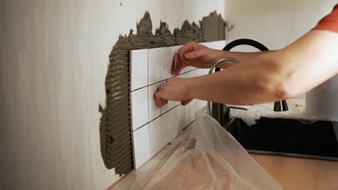 Professional tiler installing white ceramic tiles on a kitchen backsplash over Stock Footage 344565485