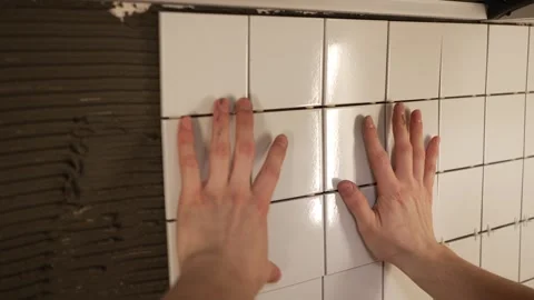 Professional tiler installing white ceramic tiles on a kitchen wall using tile Stock Footage 344566476