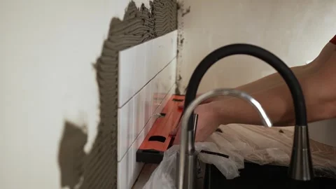 Professional tiler installing white ceramic tiles on a kitchen wall using a Stock Footage 344566605