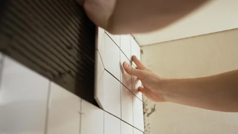 Professional tiler meticulously laying white ceramic tiles on a bathroom wall Stock Footage 344565337