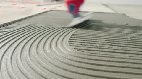 Professional tiler spreading tile adhesive with a notched trowel before Stock Footage 338991904