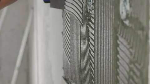 Professional tiler spreading tile adhesive on a wall before installing tiles Stock Footage 340935190