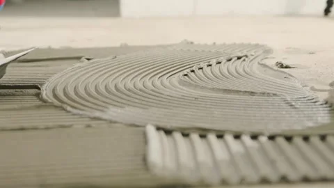 Professional tiler spreading tile adhesive with a notched trowel on the floor Stock Footage 344059214