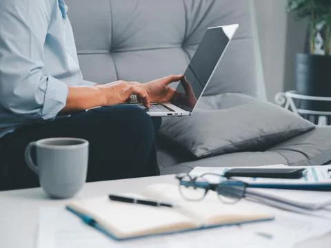 Professional using laptop on sofa with coffee cup, open notebook, glasses, .. Stock Photos