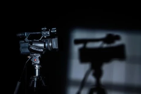 Professional video camera on tripod with shadow in dark studio Stock Photos