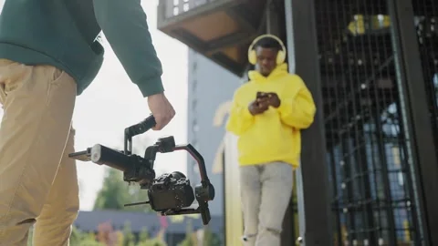 Professional videographer with camera on stabilizer shoots dark skinned young Stock Footage 244490674