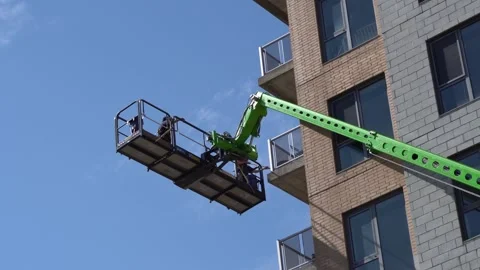 A professional window cleaner on a lime green aerial work platform reaches Stock Footage 334563749