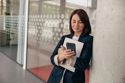 Professional woman checking smartphone while holding documents in modern office Stock Photos