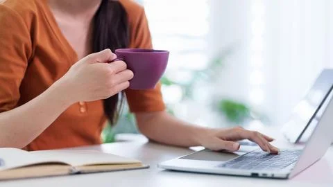 Professional woman drinking coffee while working on laptop computer at home.. Stock Photos
