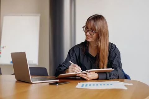 A Professional Woman Engaged in Work Using Laptop and Taking Notes within Modern Stock Photos