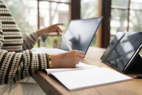 Professional Woman Taking Notes While Working on Laptop at Modern Office Desk Stock Photos