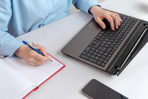 Professional woman writing notes while working on laptop in bright office e.. Stock Photos