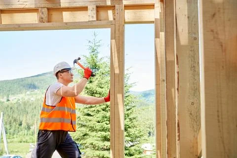 Professional worker, builder standing, holding hammer and wooden gilder, beating Foto stock