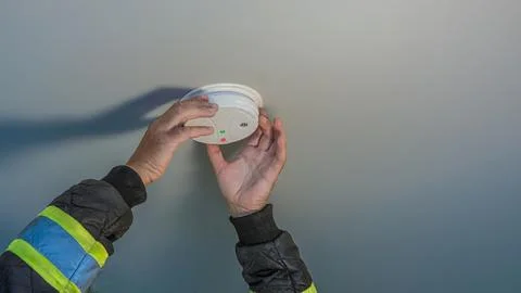 Professional worker installing or testing a smoke detector on a ceiling Stock Photos