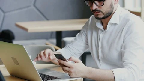 Professional worker sitting in cafe and using his phone while taking off the Stock Footage 112987086