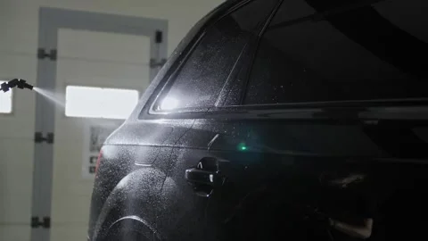 A professional worker washes the right rear side of a black SUV at a car wash. Video stock 244831067