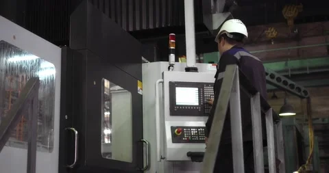 A professional working man in a helmet stands behind a CNC machine. Stock Footage 166148254