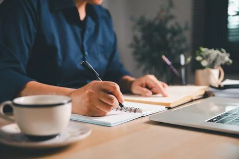 Professional writing study notes while reading an open book beside a laptop.. Foto stock