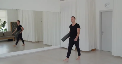 Professional yoga trainer walks into class holding mat preparing for training Stock Footage 156765126