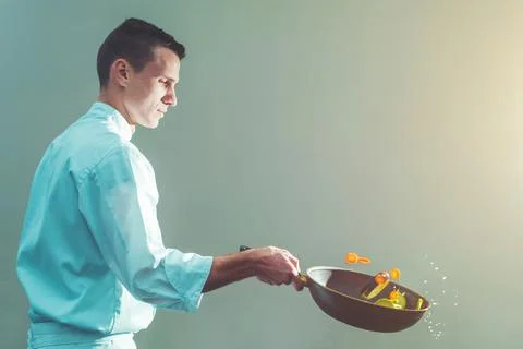 Professional young chef preparing and flipping vegetables in a frying pan, pr Stock Photos