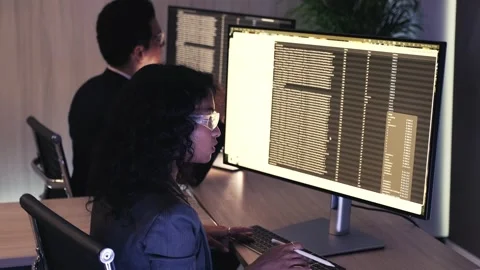 Professionals analyzing coding data on dual monitors in a dim modern office Stock Footage 318578693