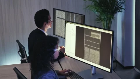 Professionals analyzing coding data on dual monitors in a dim modern office Stock Footage 326726986
