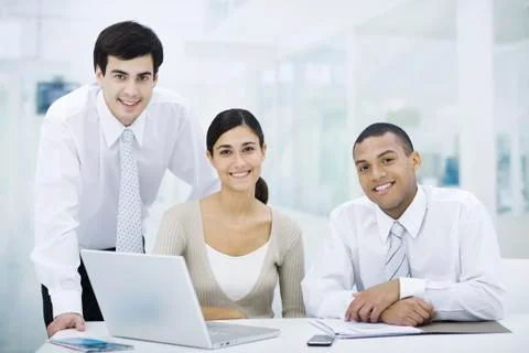 Professionals gathered around laptop computer, smiling at camera Stock Photos