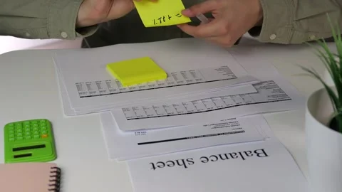 A professionals hands cross-reference figures between a calculator and printed 스톡 동영상 316458856