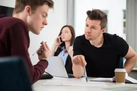 Professionals Planning While Colleague Using Smart Phone In Offi Stock Photos