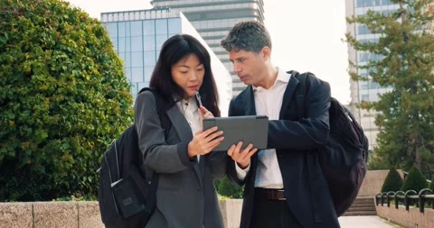 Professionals review data on a tablet while walking in a city park Vidéo 297708656