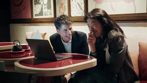 Professionals sharing a joyful conversation in a cozy cafe setting with a laptop 库存影片 305982743