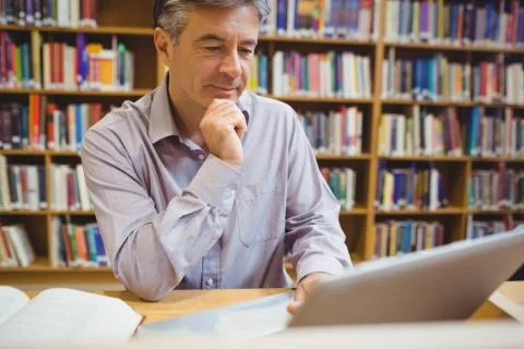 Professor sitting at desk using laptop 스톡 사진