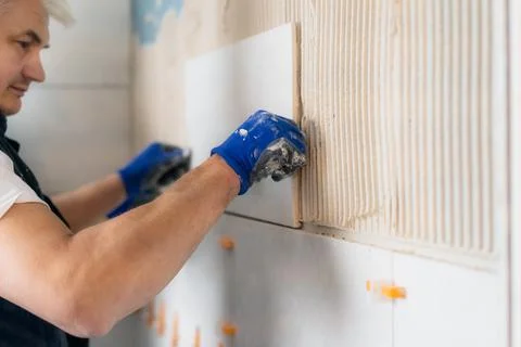 Proffesional tiler installing wall tile at home. Workers laying tiles on a Stock Photos