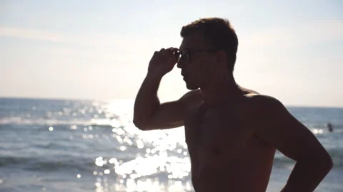 Profile of athletic guy in sunglasses jogging along sea coast. Young sporty man Video stock 330937007