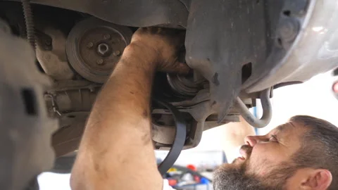 Profile of bearded auto mechanic working underneath a lifting vehicle at garage Stock Footage 307385001