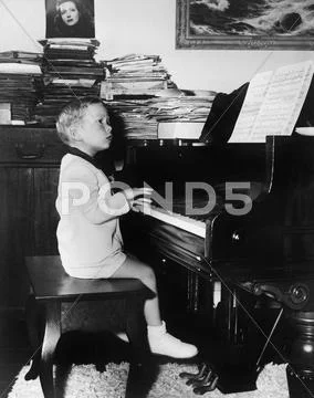 Profile of a boy sitting on a stool and playing a piano Stock Photos