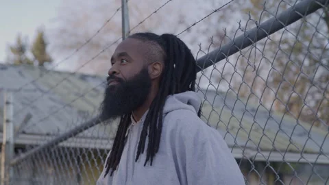Profile of Diverse Man with Dreadlocks and Beard Standing by Fence at Sunset Stock Footage 270397720