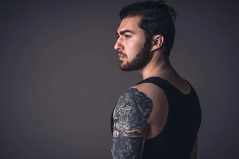 Profile of handsome guy with tattoo in studio. Caucasian strong man on black Stock Photos