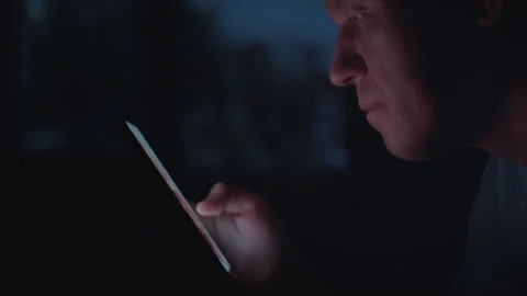 Profile of a mans face against a window at night, looking at apps on mobile Stock Footage 314523833