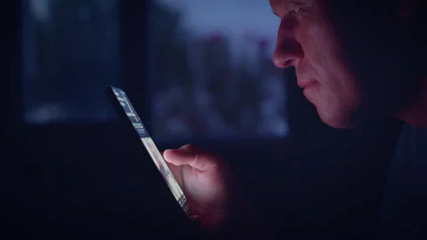 Profile of a mans face against a window at night, looking at apps on his mobile Stock Footage 315956736