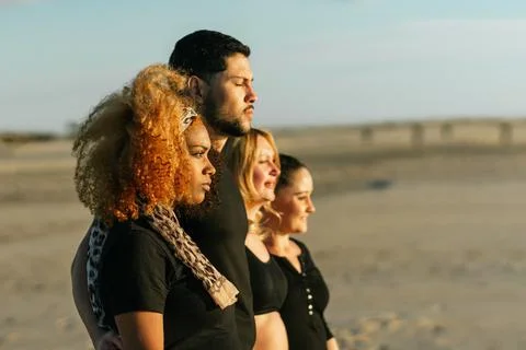 Profile of a multicultural yoga class group standing inline on a beach Stock Photos