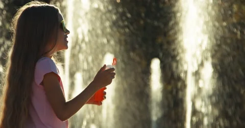 Profile portrait girl blowing soap bubbles against fountain Stock Footage