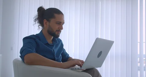 Profile shot of modern freelancer typing on laptop sitting in armchair in light Video stock 112140573