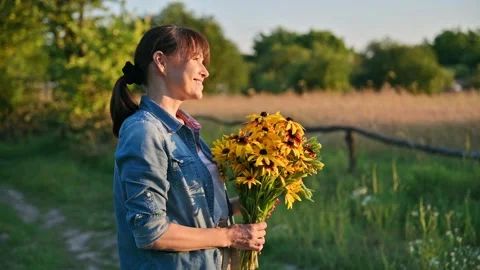 Profile view, happy middle aged woman with flowers looking at setting sun Stock Footage 246290792