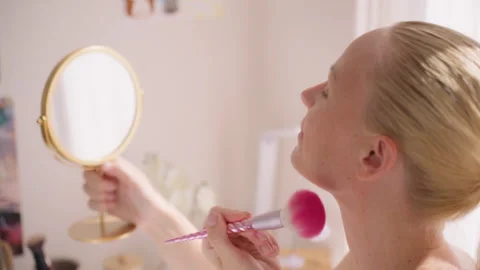 Profile view of  woman applying makeup with pink brush, looking into handhe.. Stock Footage 337058954