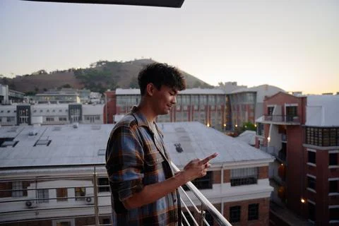 Profile view of young multiracial man in shirt using phone on balcony of Stock Photos